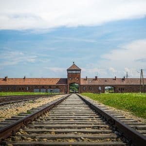 Las vías del tren conducen a la entrada de un complejo de edificios de ladrillo con una torre de vigilancia central bajo un cielo nublado.