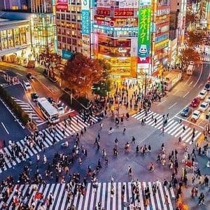 Una veduta aerea di un trafficato incrocio cittadino di notte, con folle che attraversano la strada tra il traffico e alti edifici con insegne al neon.