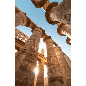 Vista dal basso di imponenti colonne di pietra con geroglifici egizi, con il sole che splende in un cielo azzurro e limpido.