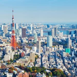 Vista aerea di un vasto paesaggio urbano caratterizzato da una prominente torre a traliccio rossa e bianca, con l'oceano visibile in lontananza.