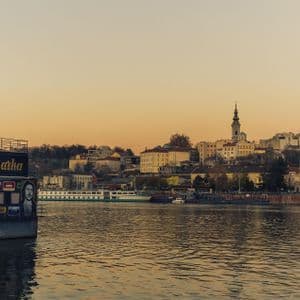El bar flotante Zappa Barka atracado en un río con un paisaje urbano en la orilla opuesta bajo un cálido cielo al atardecer.