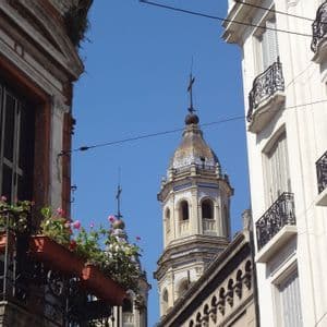Una vista dal basso di due campanili di chiesa con cupole a tegole, incorniciati da edifici residenziali con balconi, contro un cielo azzurro limpido.