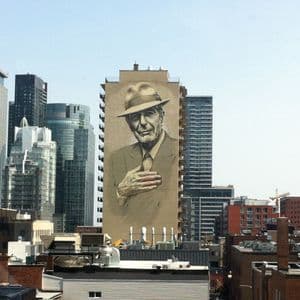 Une grande fresque murale d'un homme en fedora, la main sur le cœur, peinte sur un haut bâtiment, entourée d'un paysage urbain dense.