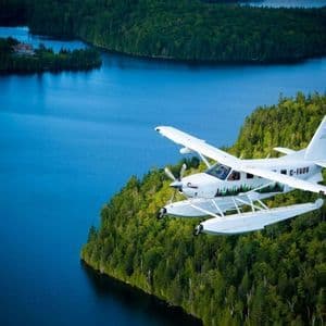 Un hydravion blanc à flotteurs survolant un grand lac bleu, entouré de forêts vertes et denses.