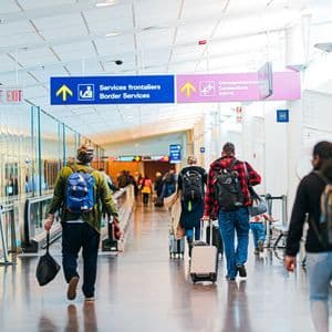 Un groupe WeRoad de voyageurs avec sacs à dos et bagages traversant un terminal d'aéroport lumineux, suivant les panneaux.