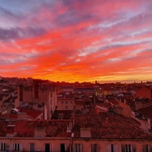 Un paysage urbain tentaculaire avec des toits en terre cuite illuminés par un coucher de soleil vibrant, orange et rouge.