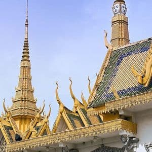 Les flèches dorées ouvragées et les toits de tuiles d'un temple traditionnel d'Asie du Sud-Est sous un ciel bleu clair.