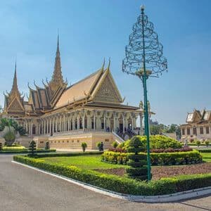 Un palais orné avec un toit doré et des flèches se dresse derrière un jardin bien entretenu doté d'un chemin pavé, sous un ciel bleu clair.