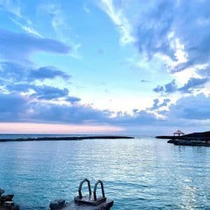 Una escalera metálica en un muelle rocoso que lleva a una ensenada tranquila bajo un cielo nublado al atardecer.