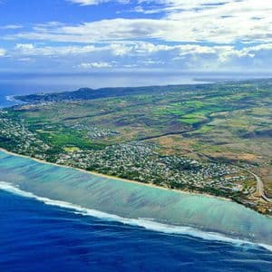 Eine Luftaufnahme einer tropischen Küste mit grünen Feldern und Städten neben einem türkisfarbenen Ozean mit weißen Wellen.