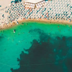 Una vista aerea di una spiaggia affollata con persone che nuotano in acqua turchese e si rilassano sotto ombrelloni colorati sulla sabbia.