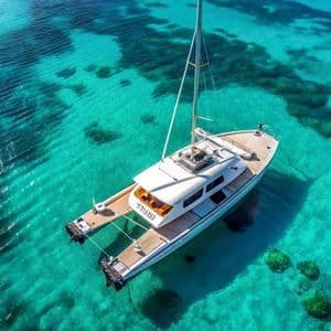 Una vista aerea di un catamarano bianco ancorato in vibranti acque turchesi, con la barriera corallina poco profonda visibile sotto.