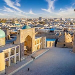 Vue aérienne d'une place historique avec un dôme turquoise et un haut minaret au lever du soleil.
