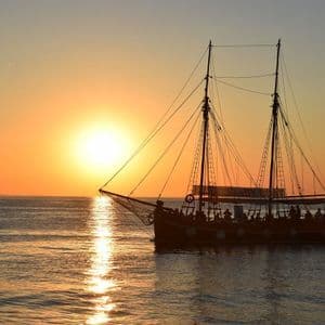 Eine silhouettierte Galeone mit einer WeRoad Gruppenreise an Bord segelt bei einem leuchtend orangefarbenen Sonnenuntergang über den Ozean.