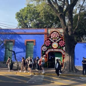 Un groupe WeRoad fait la queue sur un trottoir face à l'entrée d'un bâtiment bleu éclatant orné d'une grande arche florale.