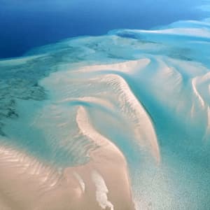 Aerial view of white sandbanks creating curved patterns in shallow turquoise water, bordering a deep blue sea.