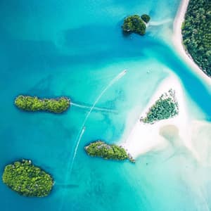 An aerial top-down view of motorboats creating wakes in turquoise water between small, lush green islands and white sandbanks.