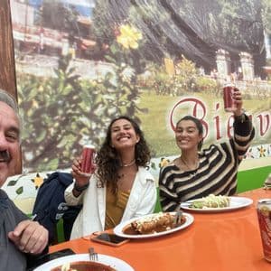 Voyage de groupe WeRoad: trois personnes souriantes trinquent et mangent au restaurant.