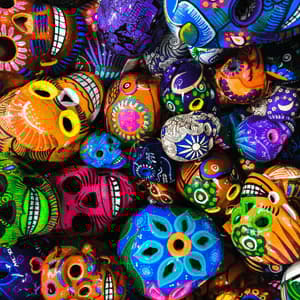 Vue plongeante rapprochée de nombreux crânes Calavera colorés, peints à la main, avec des motifs floraux et géométriques complexes.