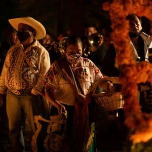 Un groupe de personnes en vêtements traditionnels et masques se rassemble la nuit autour d'une grande croix faite d'œillets d'Inde oranges.
