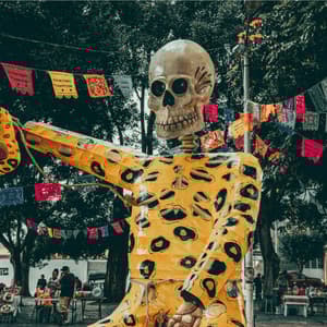 Une grande marionnette squelette au motif jaguar tenant un masque lors d'un festival en plein air avec des bannières colorées.