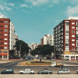 Un'ampia strada cittadina con una rotonda è affiancata da grandi palazzi residenziali in mattoni rossi sotto un cielo parzialmente nuvoloso.