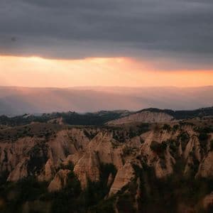Au coucher du soleil, des rayons de soleil percent les nuages sombres, éclairant un vaste paysage de formations rocheuses érodées et pointues.