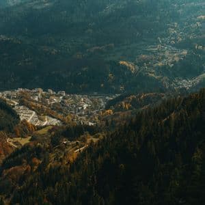 Vue plongeante sur une petite ville nichée dans une vallée montagneuse, entourée de forêts denses aux couleurs automnales.