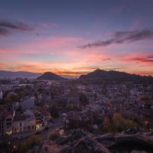 Une vue aérienne d'un paysage urbain niché entre deux grandes collines sous un ciel de coucher de soleil vibrant, rose, violet et orange.