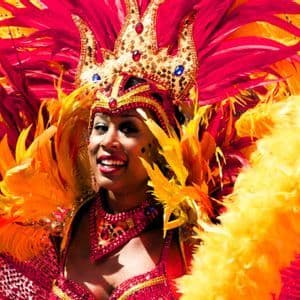 Eine lächelnde Frau mit farbenprächtigem rot-gelbem Federkopfschmuck und Paillettenkostüm für Karneval.