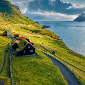 Una vista aerea di case tradizionali con tetti d'erba adagiate su una verde collina costiera vicino al mare.