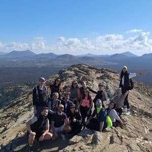 Un viaggio di gruppo WeRoad in posa per una foto su una cresta rocciosa di montagna, con un paesaggio vulcanico sullo sfondo.