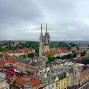 An elevated view of a cityscape featuring a large cathedral with two spires surrounded by buildings with red roofs under a cloudy sky.