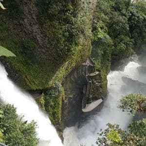 Une vue d'en haut d'une grande cascade se jetant dans une gorge verdoyante, avec un escalier en pierre sinueux à flanc de falaise.