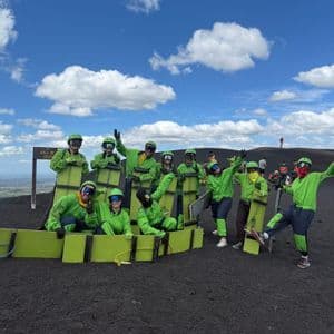 Un groupe WeRoad en équipement de protection vert vif pose pour une photo avec ses planches de volcan sur une pente sombre et graveleuse.