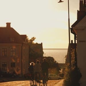 Eine WeRoad-Gruppenreise mit drei Personen, die bei einem warmen Sonnenuntergang eine Kopfsteinpflasterstraße hinunter zum Meer radeln.