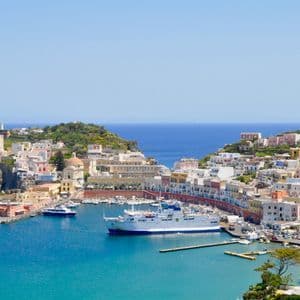 Una vista panoramica di una città di mare con edifici colorati sulle colline che si affacciano su un porto blu brillante con un grande traghetto.