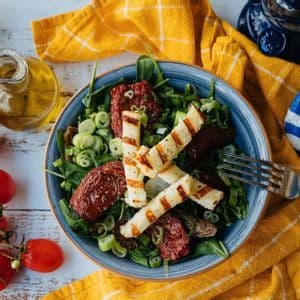 Una vista dall'alto di un'insalata con formaggio grigliato e pomodori secchi, accanto a una pietra con una bandiera greca.