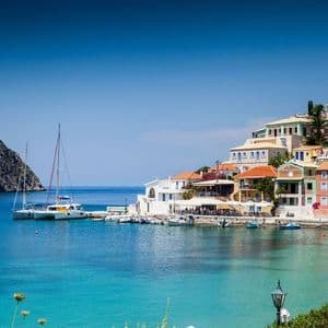 Case colorate di un villaggio marinaro costruito su una collina che si affaccia su una baia con acqua turchese e barche ormeggiate.