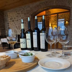 Une dégustation de vin avec quatre bouteilles de vin, des verres et des amuse-gueules disposés sur une table recouverte d'une nappe blanche.
