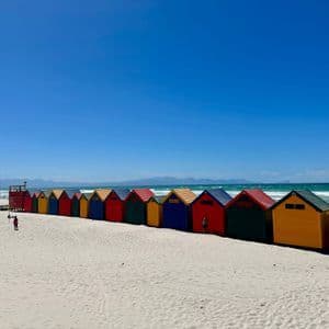 Una lunga fila di colorate capanne di legno su una spiaggia di sabbia bianca con l'oceano sullo sfondo e un cielo sereno.