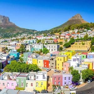 Un fitto quartiere di case dai colori vivaci si adagia su una collina sotto due grandi montagne e un cielo sereno.