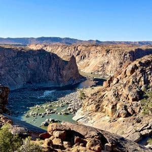 Un fiume si snoda attraverso un vasto canyon roccioso con ripide scogliere sotto un cielo azzurro e limpido.