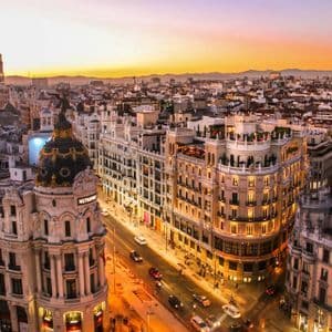 An aerial view of a cityscape at sunset, featuring the ornate Metropolis building and traffic on the street below.