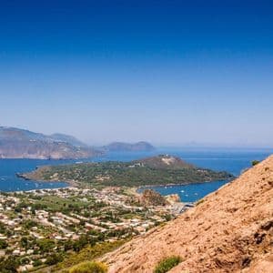 Due partecipanti a un viaggio di gruppo WeRoad si trovano su una scogliera, ammirando una città costiera e diverse isole sotto un cielo limpido e azzurro.