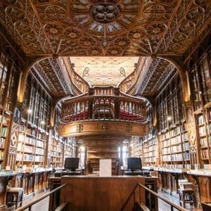 L'interno di una sfarzosa biblioteca in legno con scaffali a tutta altezza e una grande scalinata centrale curva.