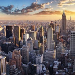 An aerial view of a dense city skyline packed with skyscrapers, illuminated by the warm light of a setting sun.