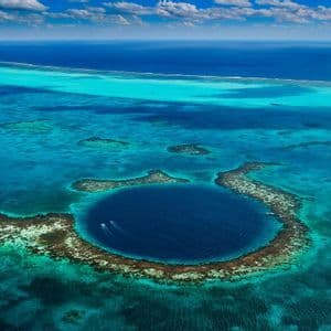 Una vista aerea di un grande, profondo buco blu marino circolare, circondato da un atollo di barriera corallina in un oceano turchese.