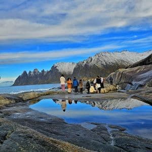 Un viaggio di gruppo WeRoad si trova su una costa rocciosa, con montagne innevate e il cielo riflesso in uno specchio d'acqua.