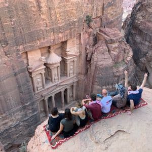 Un grupo de WeRoad se sienta en la arena roja del desierto alrededor de una tetera, con montañas al fondo durante el atardecer.